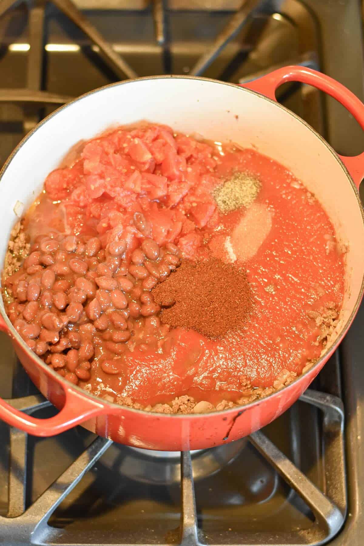 Chili powder and spices added to ground beef in a Dutch oven.