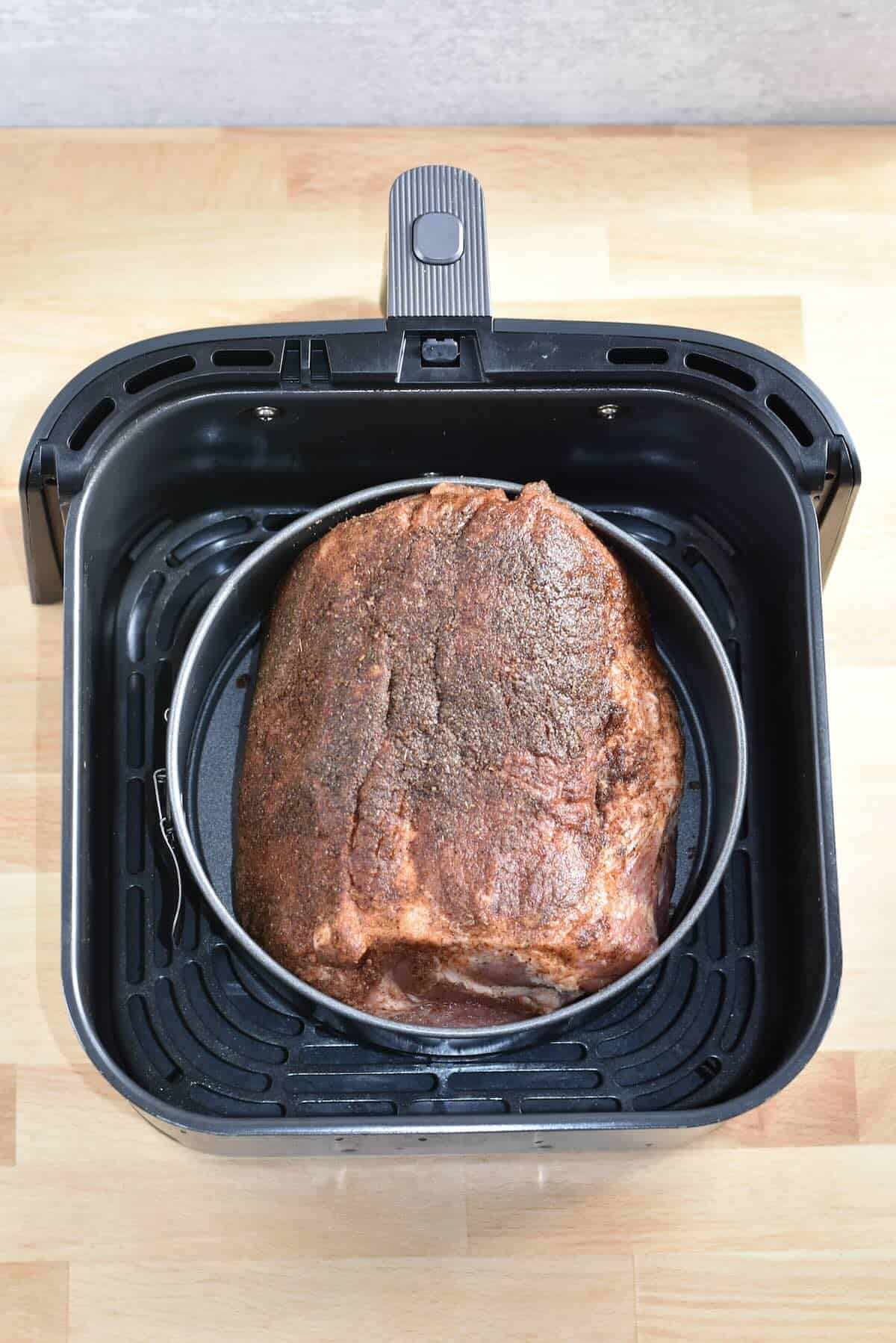 Seasoned pork shoulder cooking in an air fryer basket lined with a round pan.