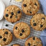 A tray of bakery style blueberry muffins cooling on a baking rack.