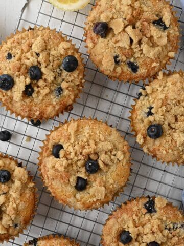 A tray of bakery style blueberry muffins cooling on a baking rack.
