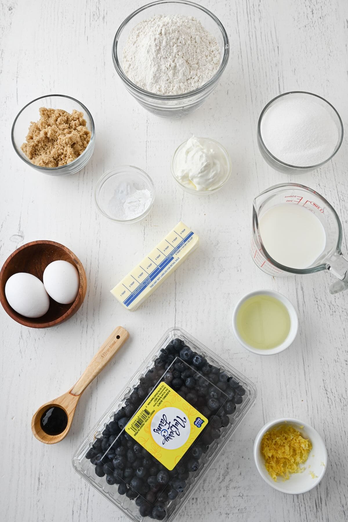 Blueberry muffin ingredients with lemon zest, sour cream and other ingredients laid on a table.