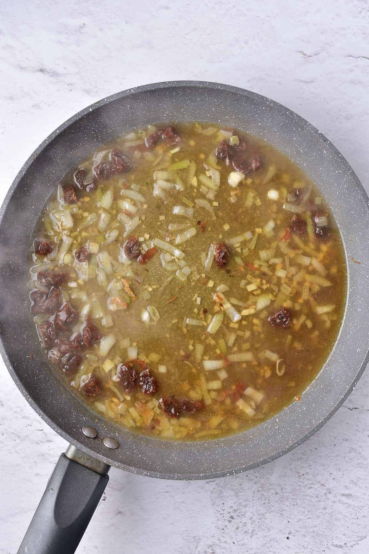 Broth and sun dried tomatoes added to the garlic and onions to build a rich sauce.