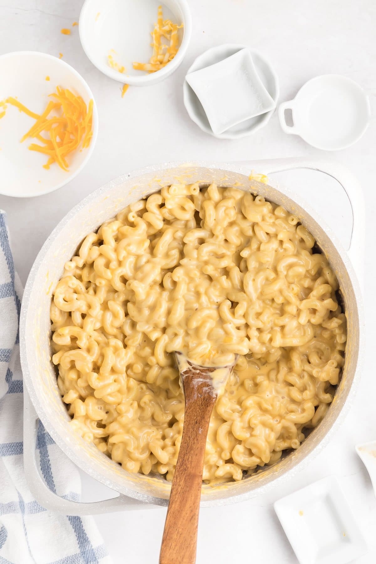 Extra creamy stovetop mac and cheese served in a large pot with a wooden spoon and bowl on the side.