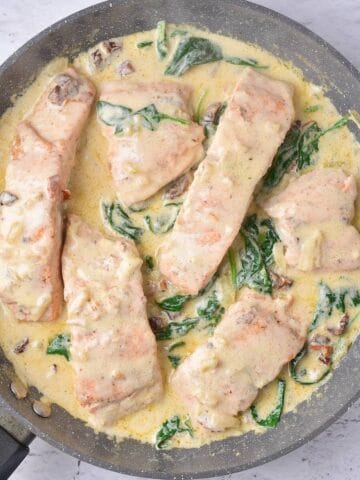 Flaky and tender salmon in a rich creamy sauce with spinach, in a skillet and ready to serve.