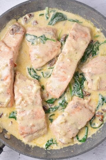 Flaky and tender salmon in a rich creamy sauce with spinach, in a skillet and ready to serve.