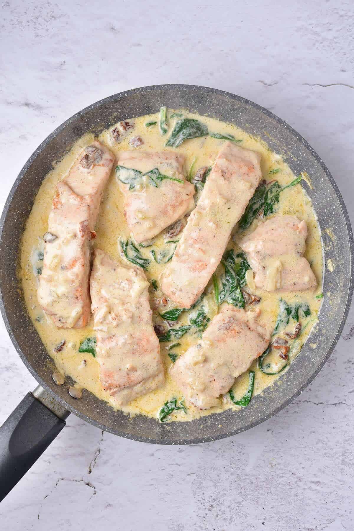 Creamy Tuscan salmon in a skillet with spinach, sun-dried tomatoes, and parmesan cream sauce.