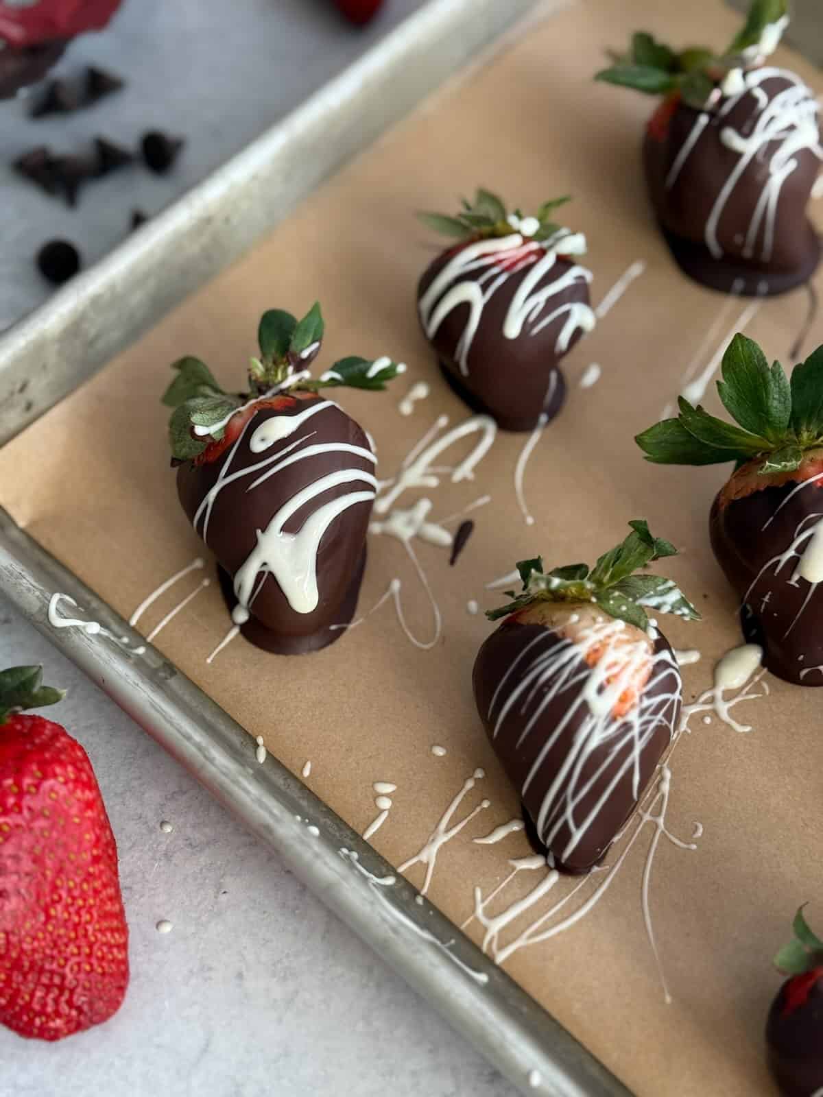 White chocolate drizzled over chocolate covered strawberries on parchment paper.