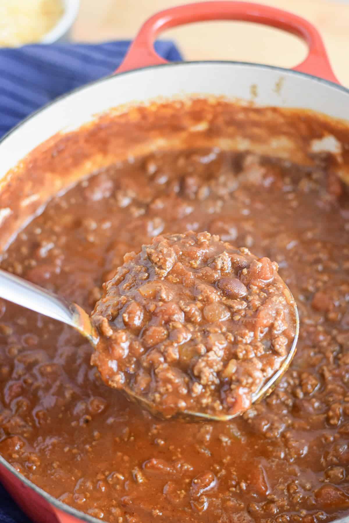 Ladle lifting thick Dutch oven chili for a crowd with ground beef and beans.
