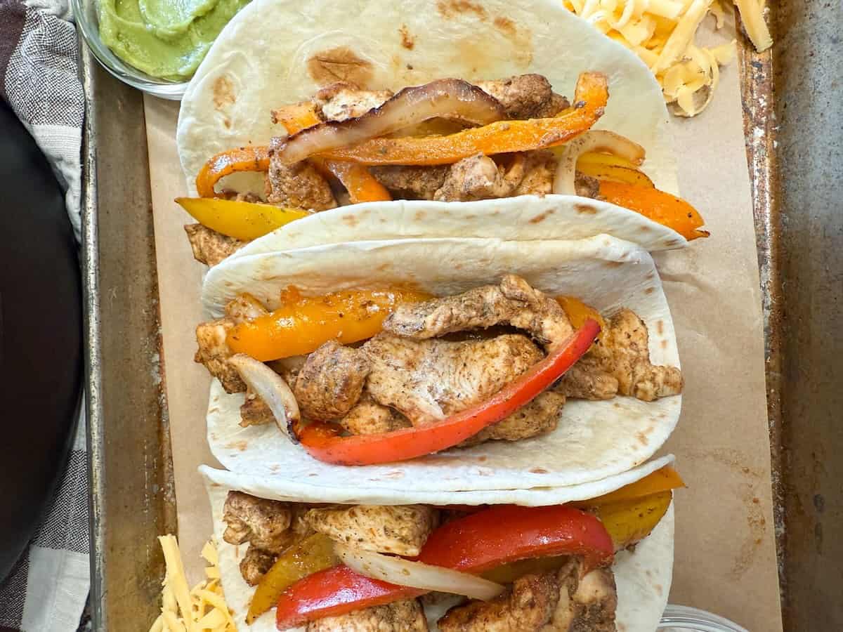 Plated chicken fajitas, ready for serving with guacamole and shredded cheese.