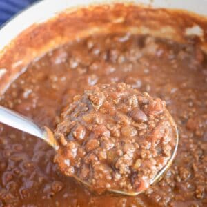 Ladle lifting thick Dutch oven chili for a crowd with ground beef and beans.