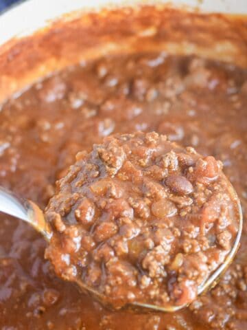 Ladle lifting thick Dutch oven chili for a crowd with ground beef and beans.