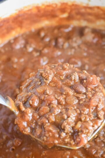 Ladle lifting thick Dutch oven chili for a crowd with ground beef and beans.