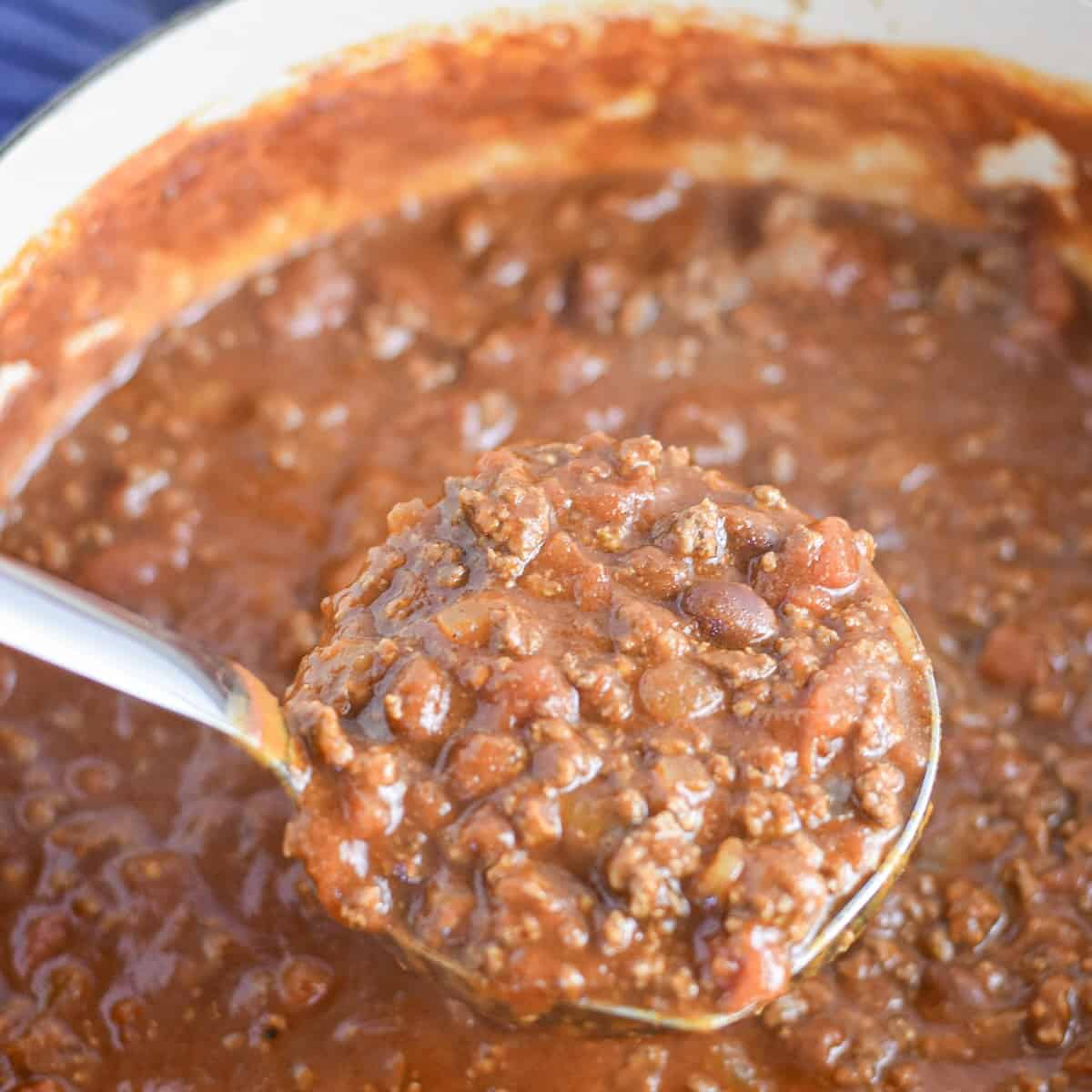 Ladle lifting thick Dutch oven chili for a crowd with ground beef and beans.