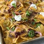 Close-up of leftover BBQ pulled pork nachos with melted cheese, barbecue sauce, pickled red onions, jalapeños, and sour cream.