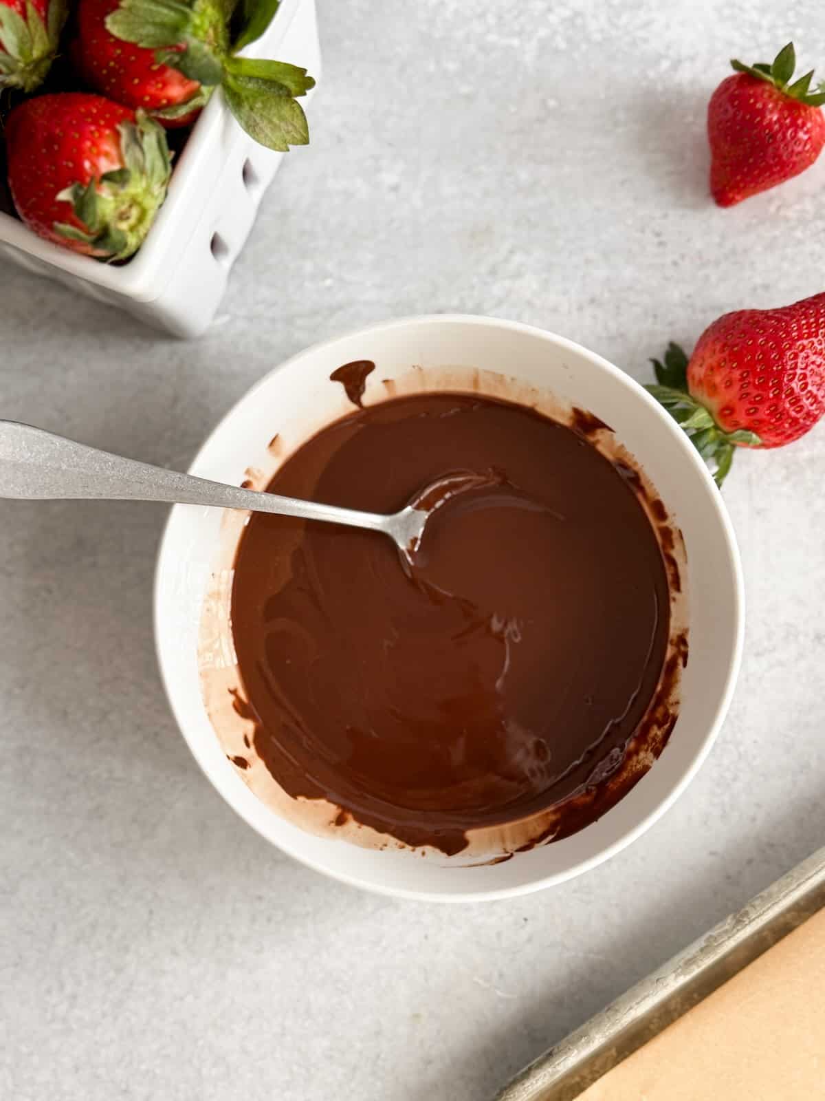 Melted chocolate stirred smooth in a microwave-safe bowl, ready for dipping strawberries.
