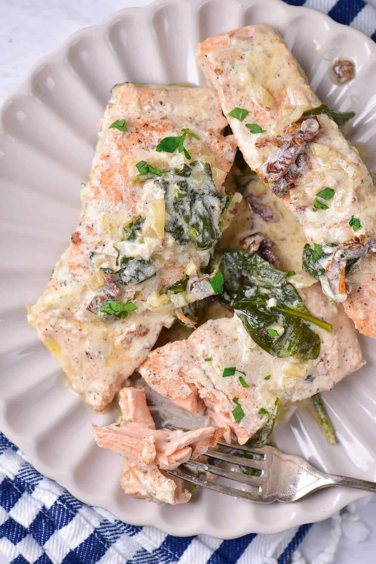 Plated Tuscan salmon topped with cream sauce and spinach with a flaky tender bite showing.
