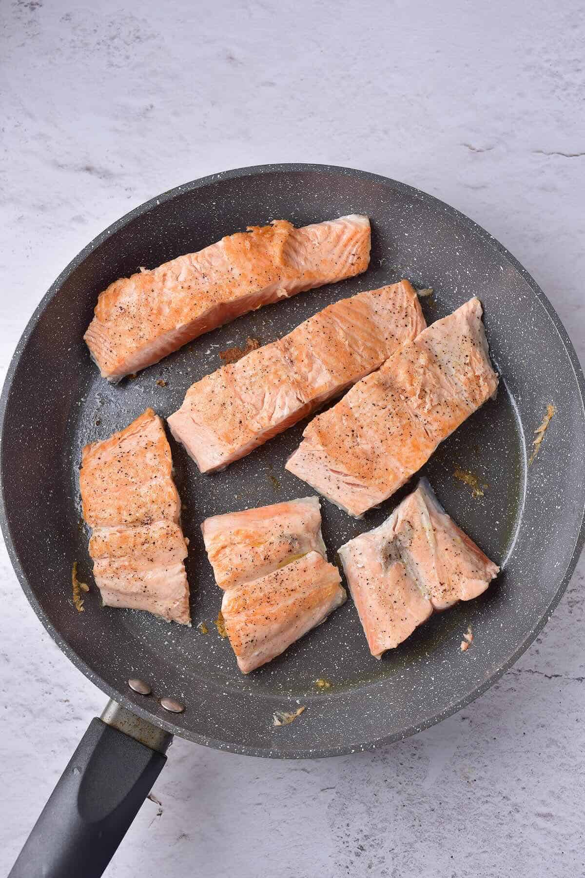 Salmon fillets searing in a skillet before adding cream sauce.