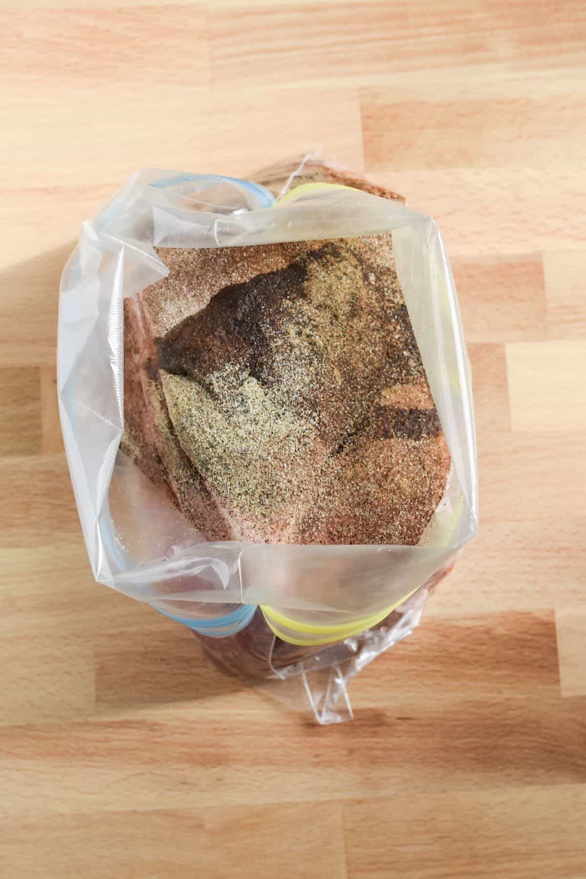 Pork shoulder coated with dry rub seasoning inside a zip-top bag before air frying.