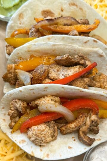 Three flour tortillas filled with chicken, bell peppers and onions.
