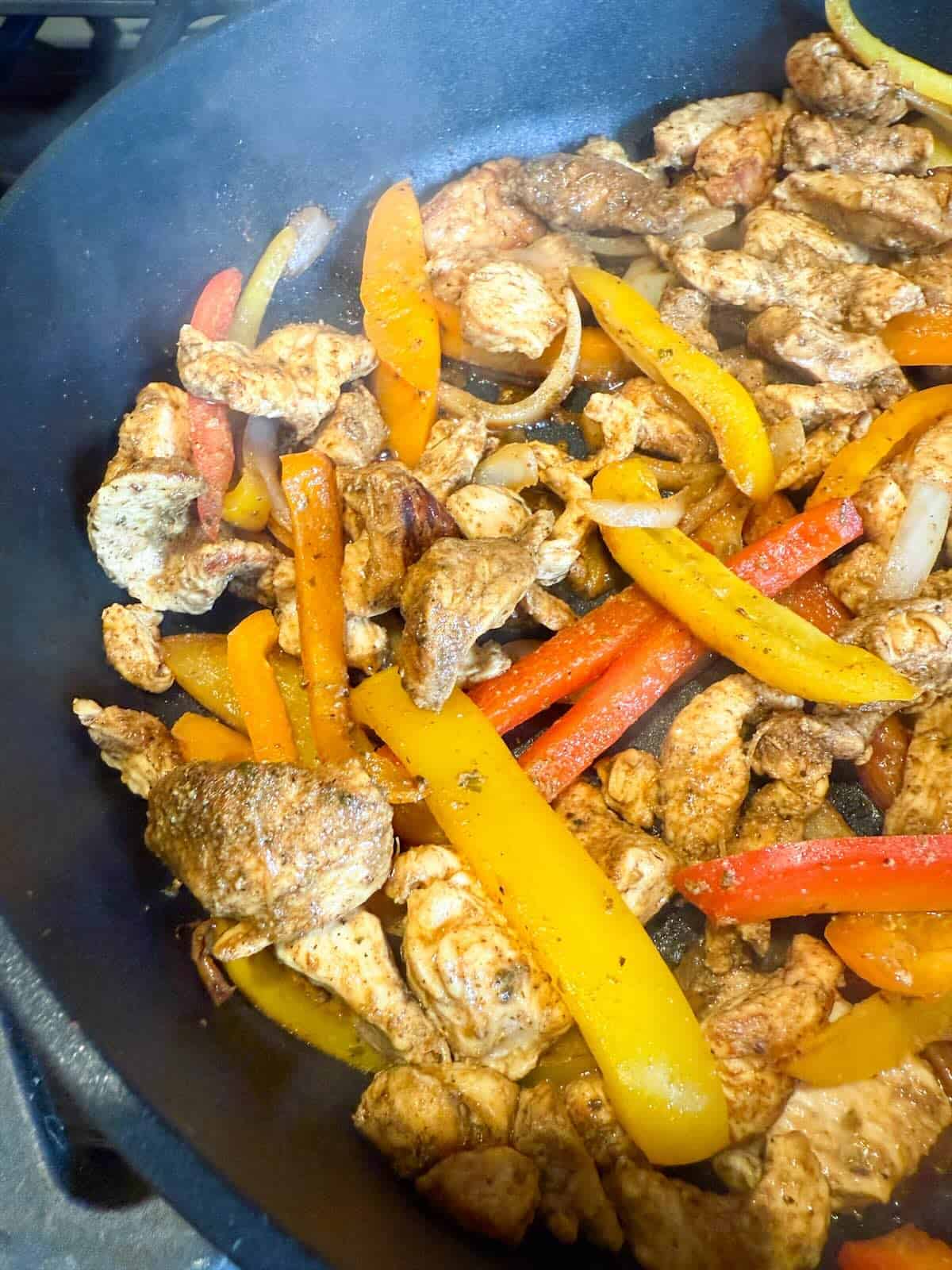 A skillet filled with seasoned chicken fajita strips and tender onions and peppers.