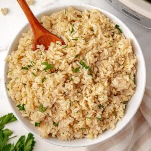 A bowl of fluffy brown rice for serving topped with fresh parsley.