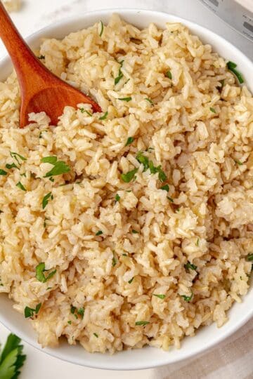 A bowl of fluffy brown rice for serving topped with fresh parsley.