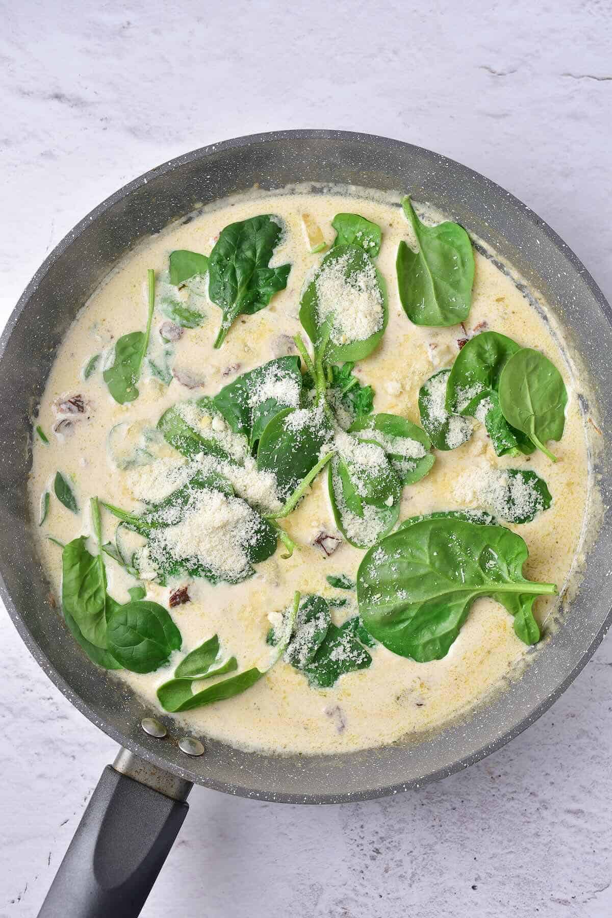 Garlic cream sauce with spinach and sun-dried tomatoes cooking in a pan.