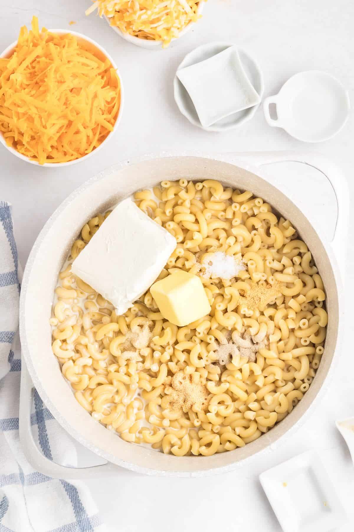 Cooked elbow macaroni in a pot with milk, cream, cream cheese and seasonings being added for stovetop mac and cheese.
