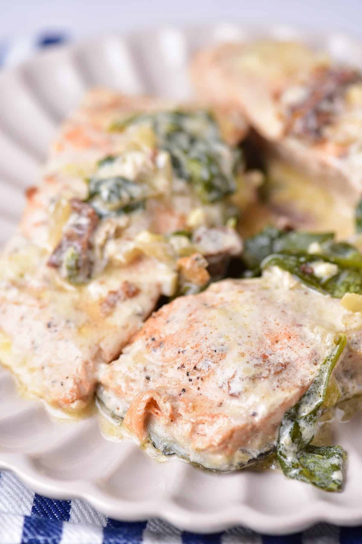Close-up of salmon fillet in garlic parmesan cream sauce with spinach and sun-dried tomatoes.
