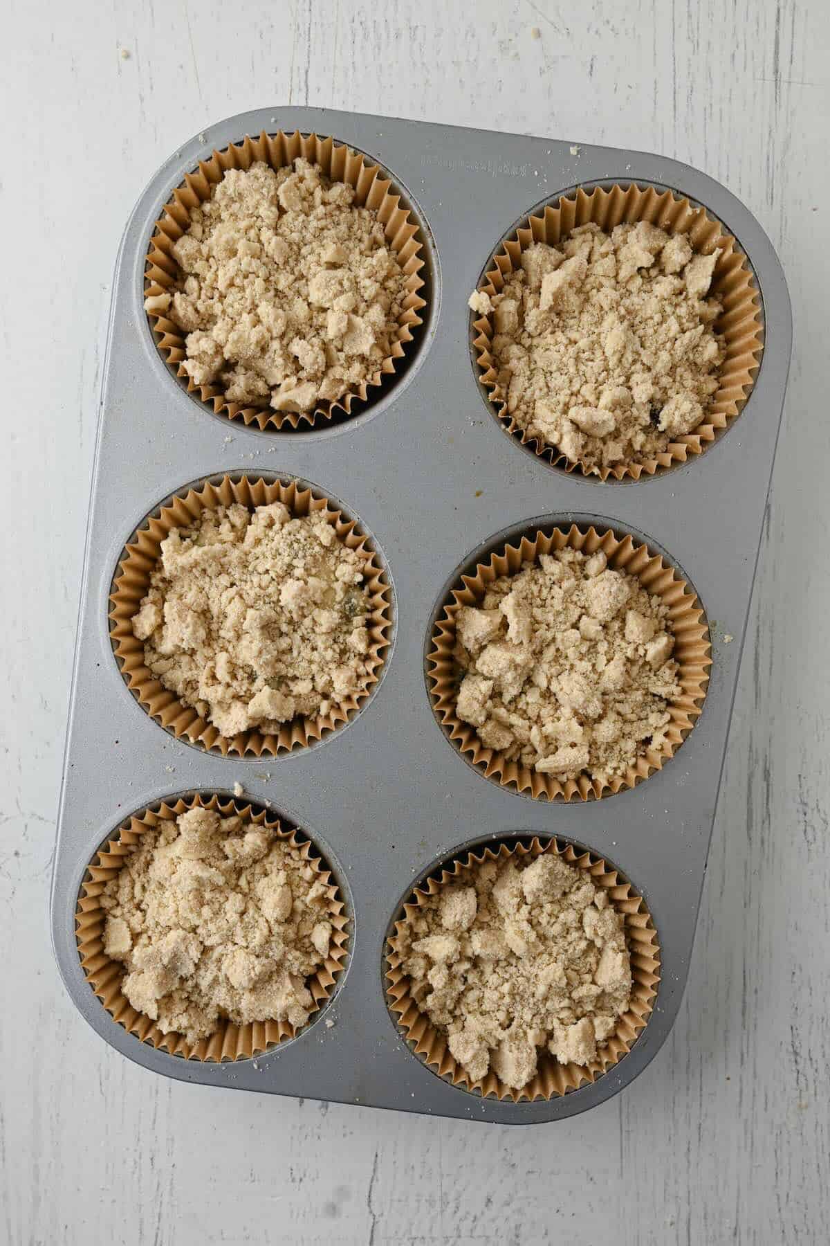 Unbaked bakery style blueberry muffins with streusel in muffin pan.