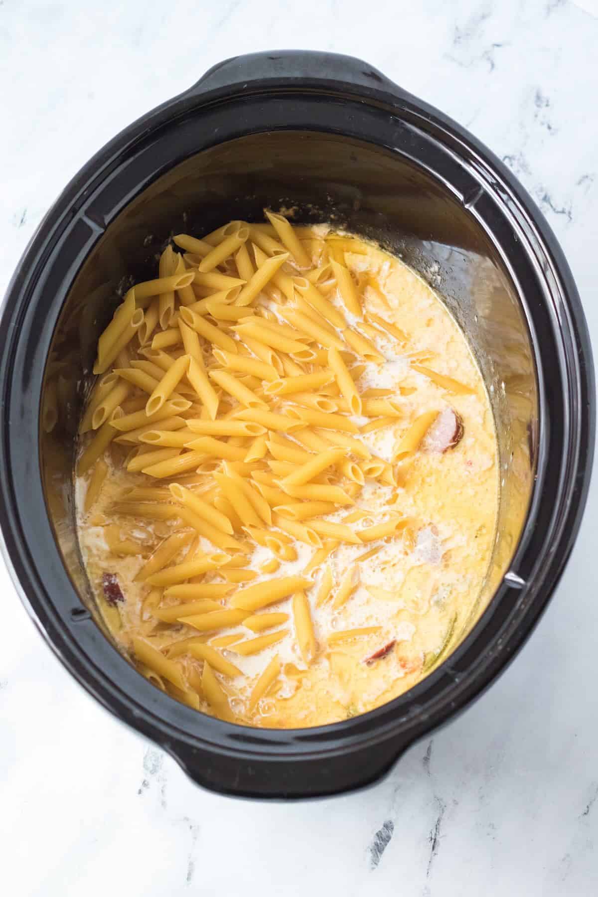 Penne pasta being added to slow cooker Cajun chicken pasta.