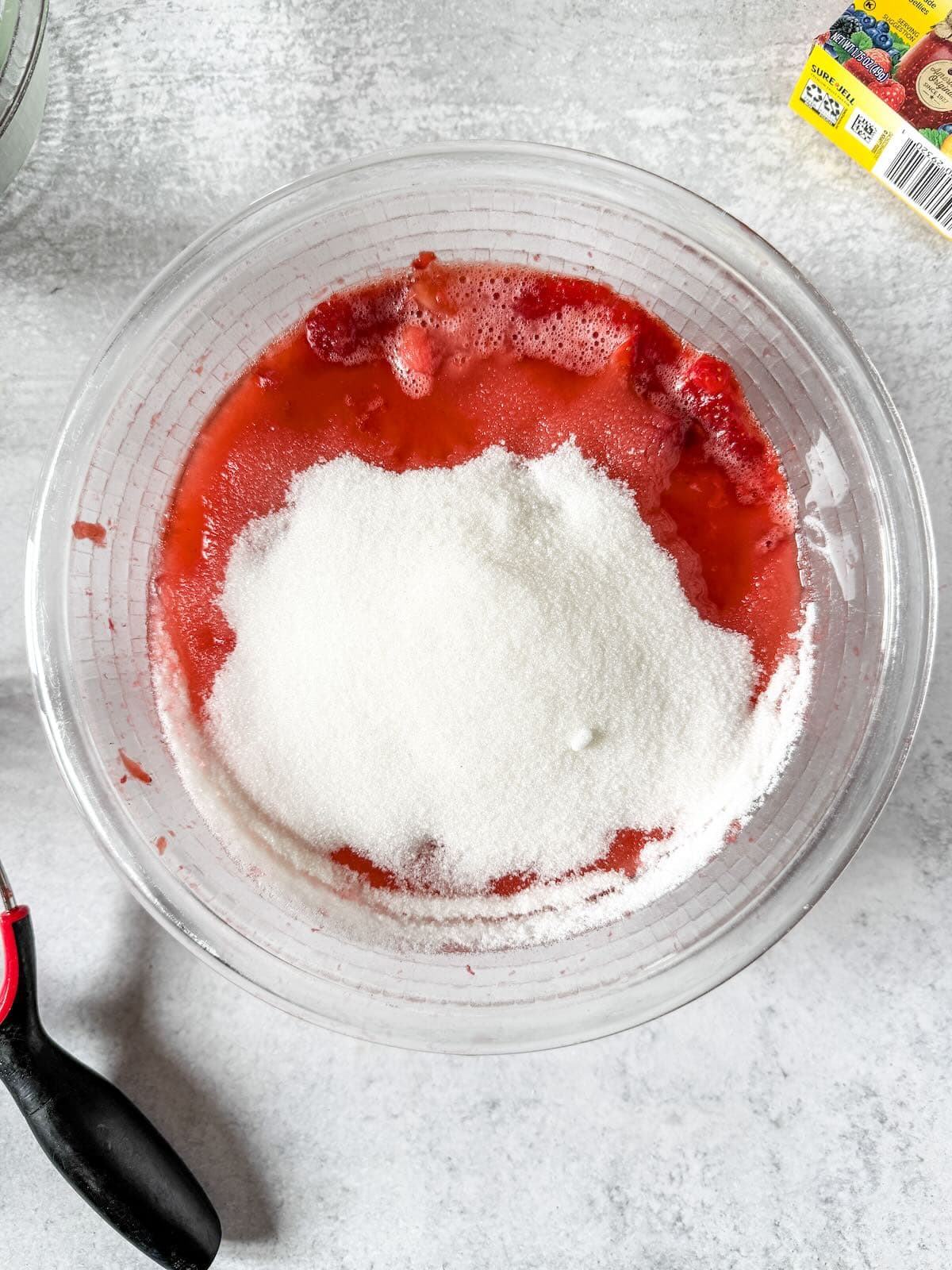 Adding sugar to crushed strawberries for strawberry freezer jam.