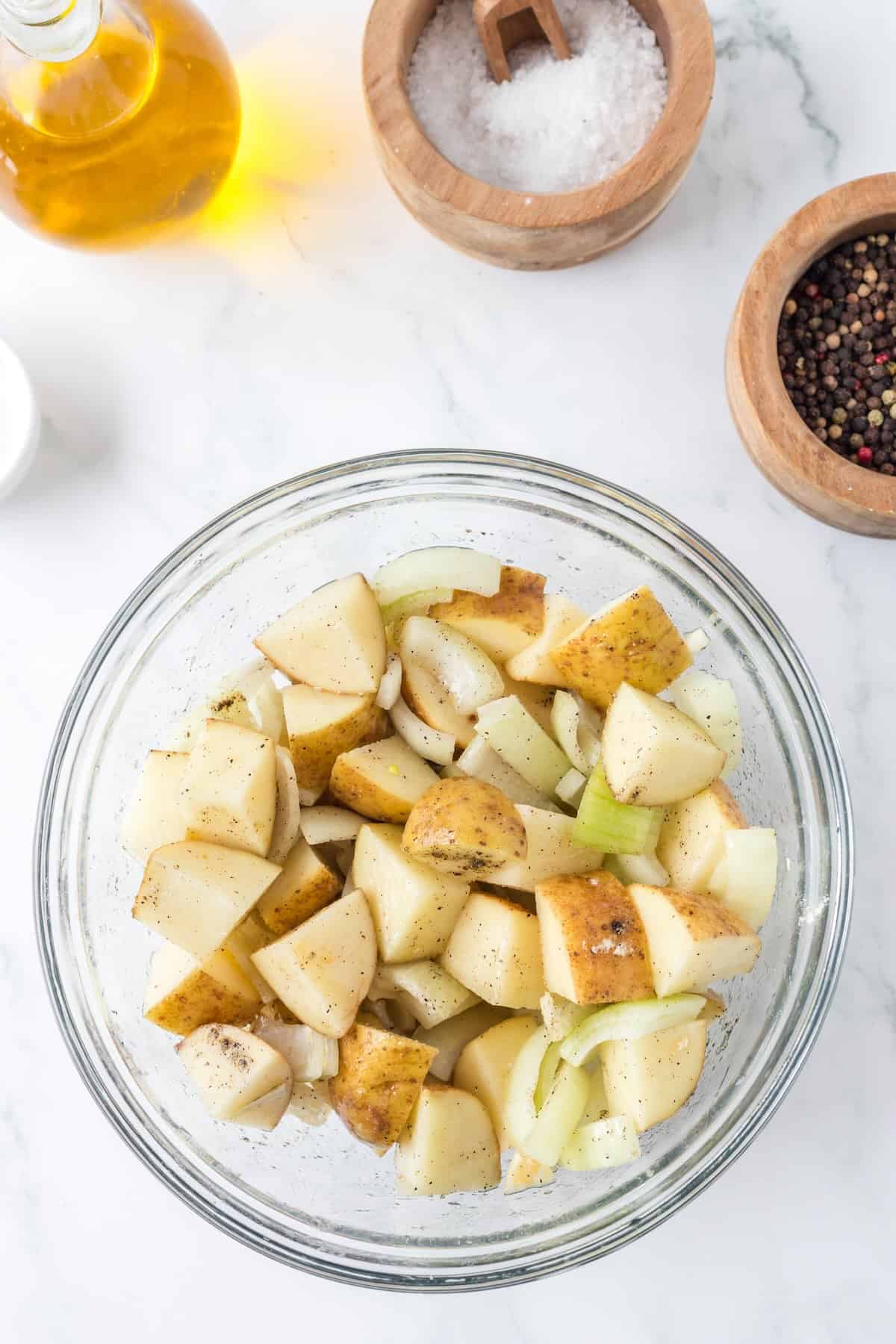 Cubed potatoes and chopped onions tossed with oil and seasoning for air fryer potatoes.