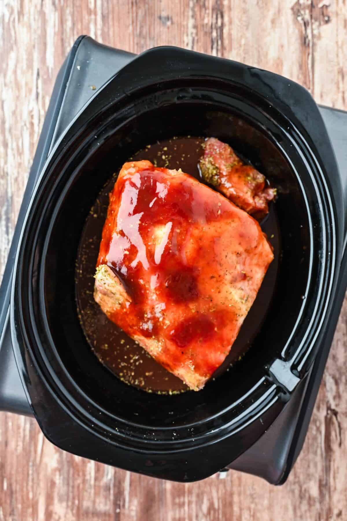 Bbq sauce poured over a pork roast before cooking low and slow in the slow cooker.