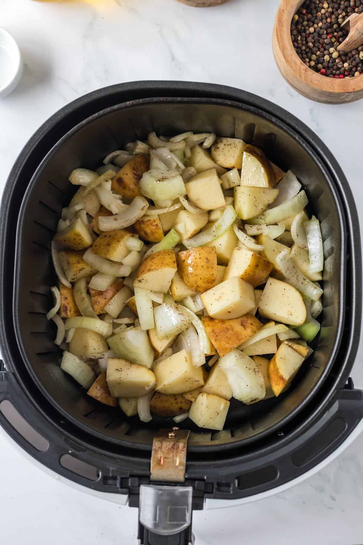 Seasoned potatoes and onions placed in air fryer basket before cooking.
