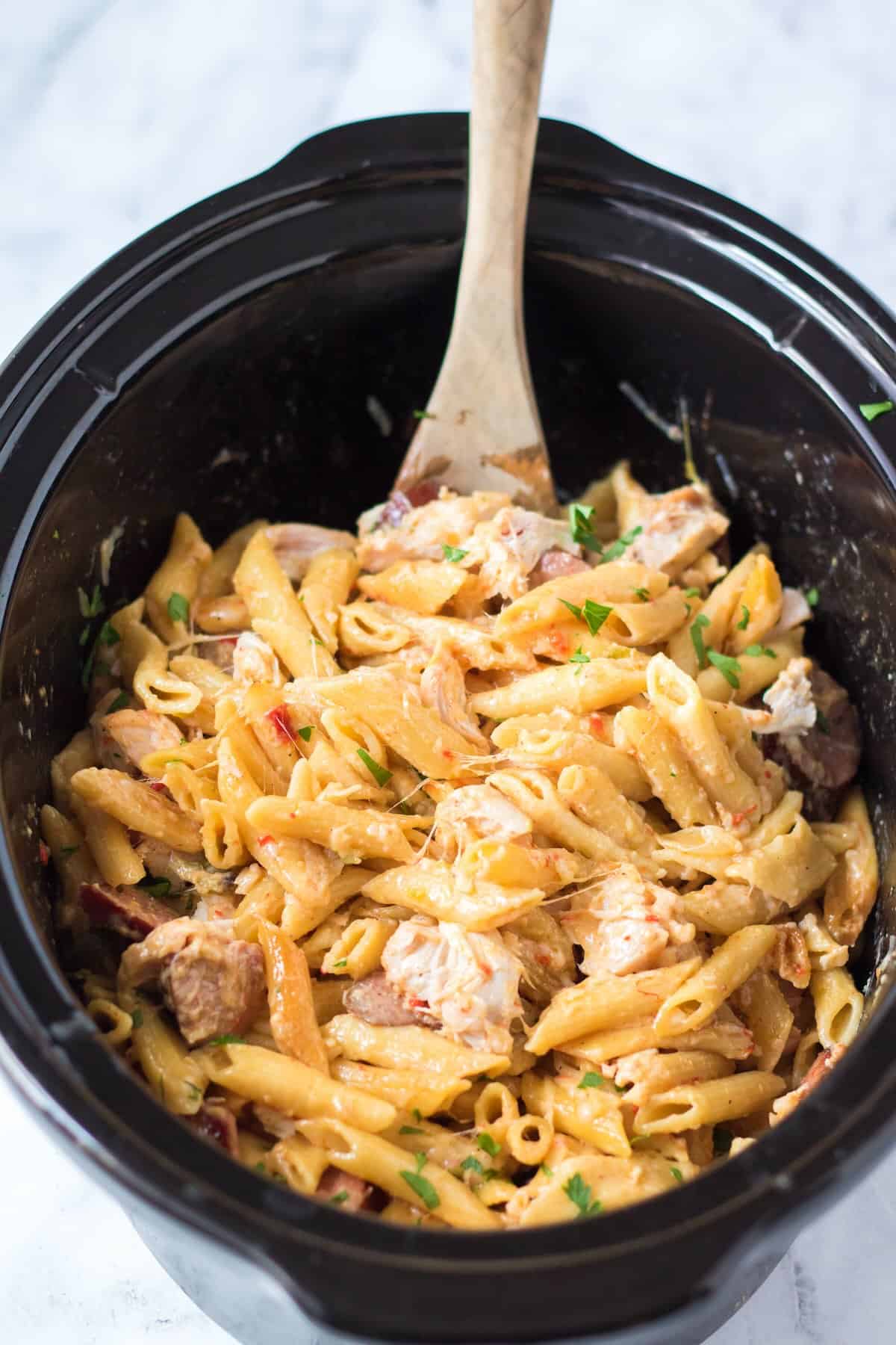 A wooden spoon serving up a cozy batch of creamy Cajun pasta with chicken and kielbasa.