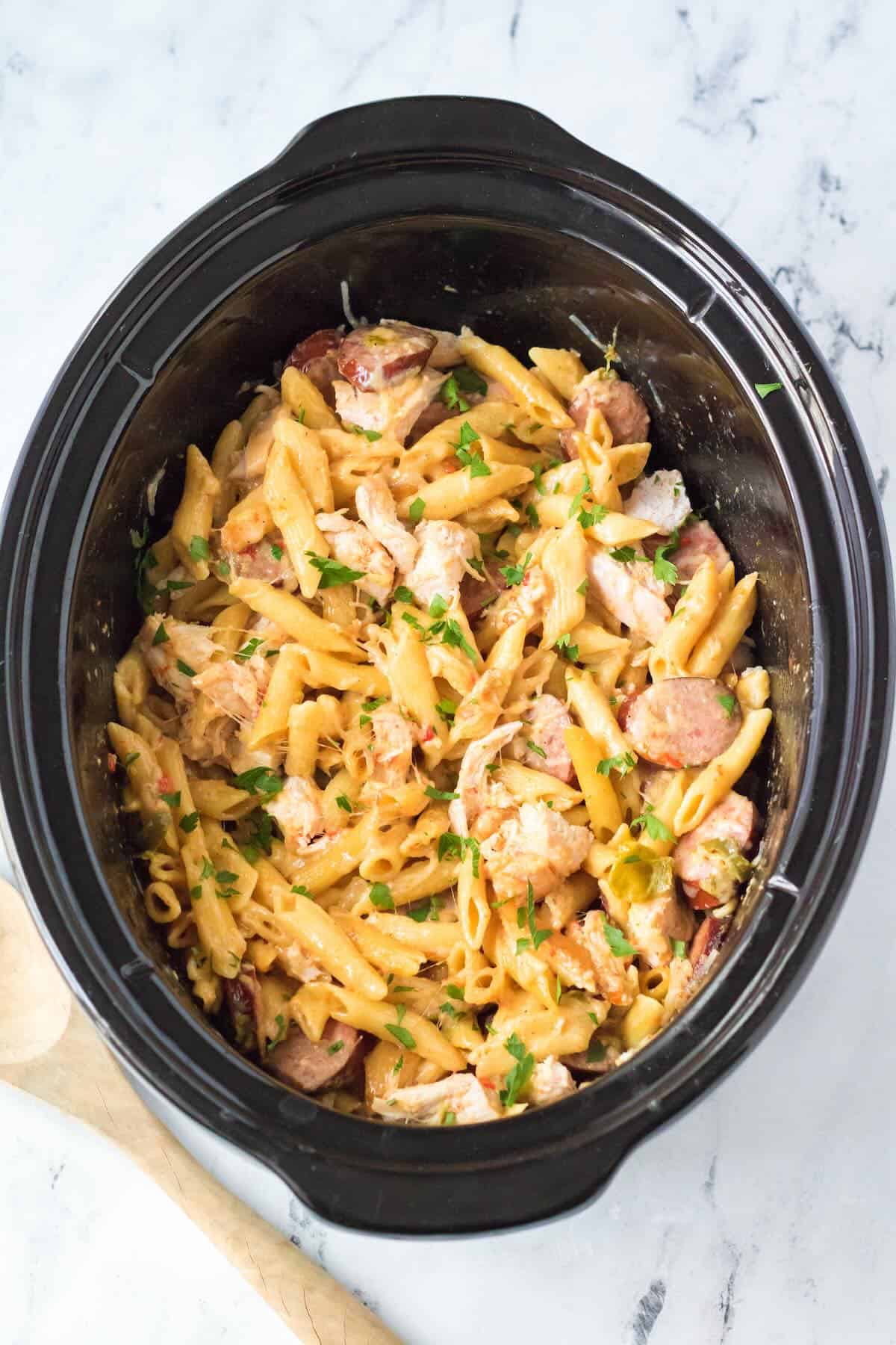 Slow cooker Cajun chicken pasta cooking with smoked sausage, peppers and creamy sauce.