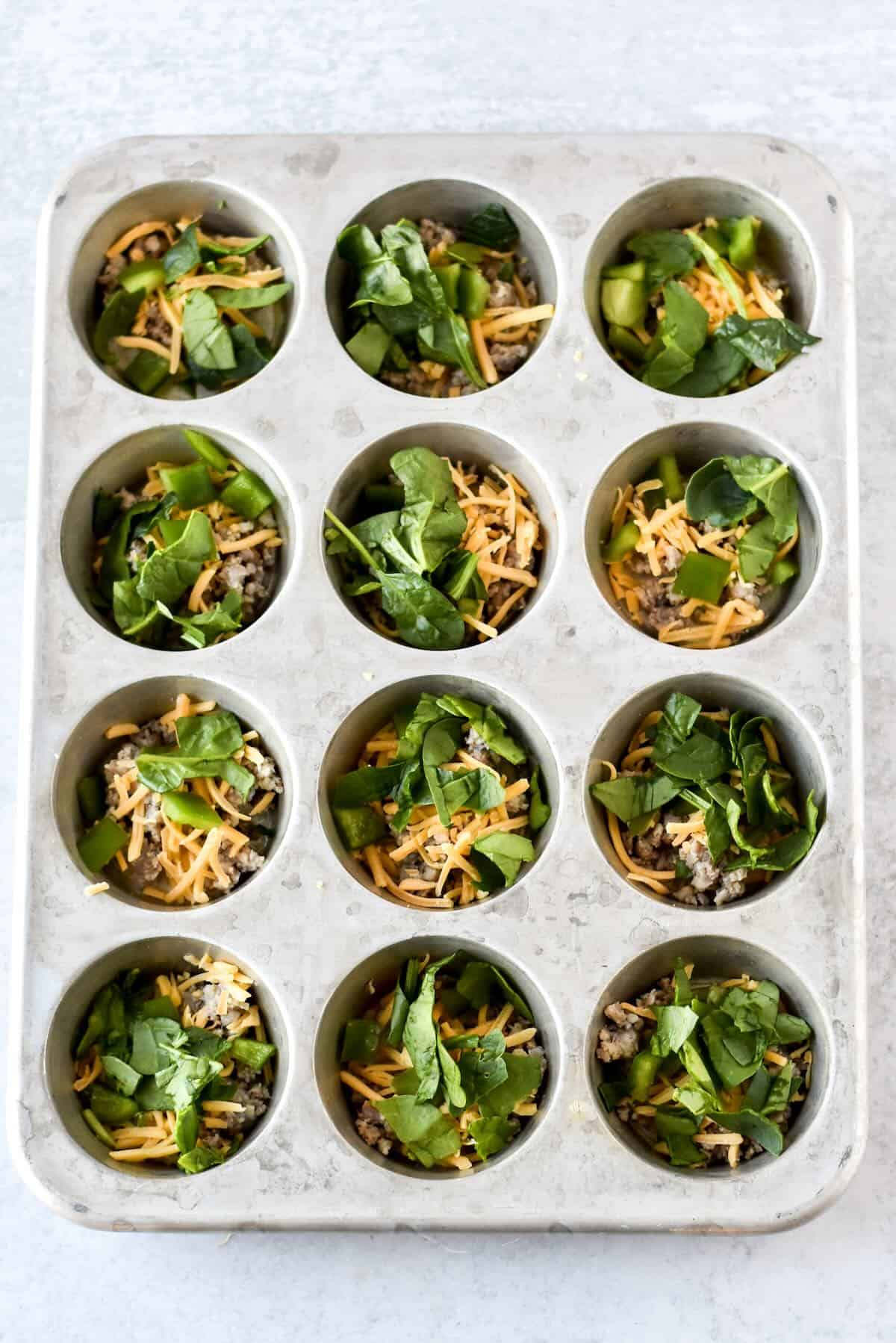 Sausage, spinach and peppers added to muffin pan for egg muffins.