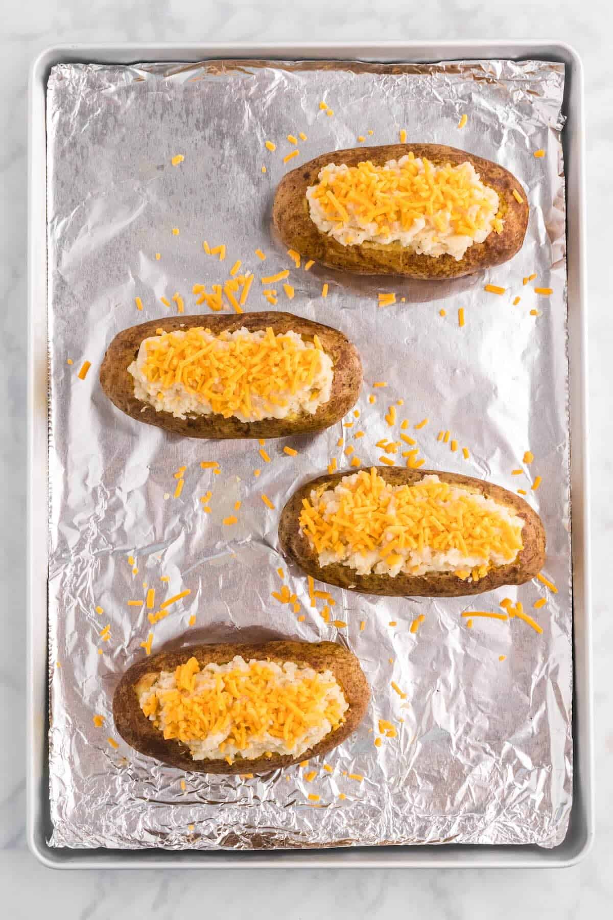 Topping stuffed potatoes with shredded cheddar cheese before the second bake.