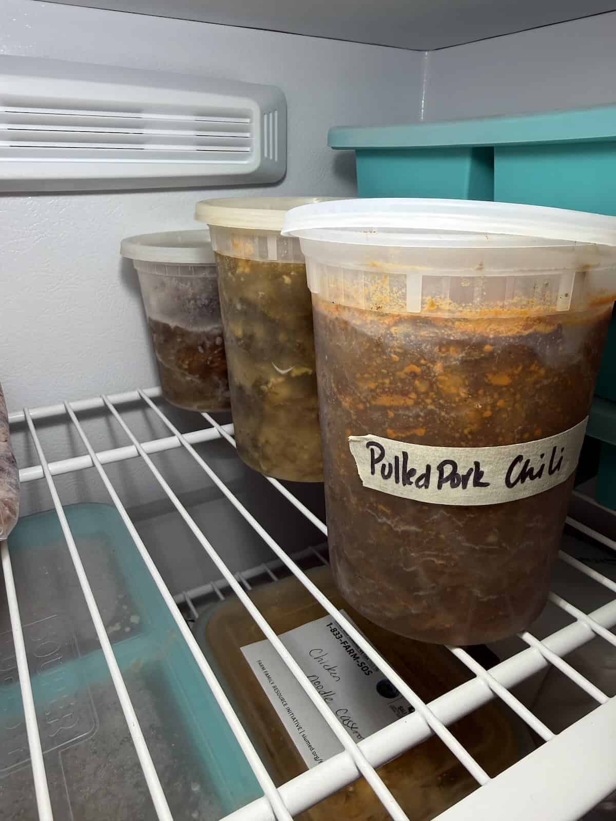 Soup and chili frozen in labeled plastic containers in freezer.