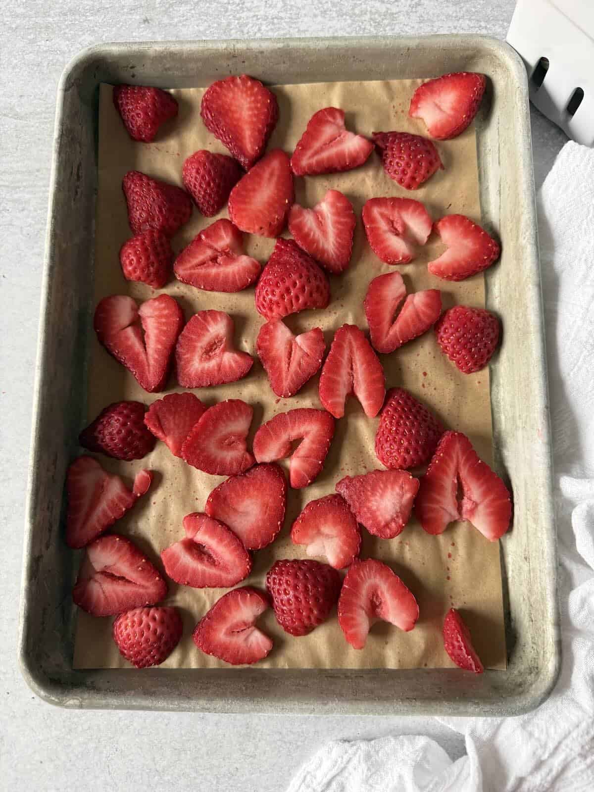 A tray of sliced strawberries frozen on a sheet pan for later.