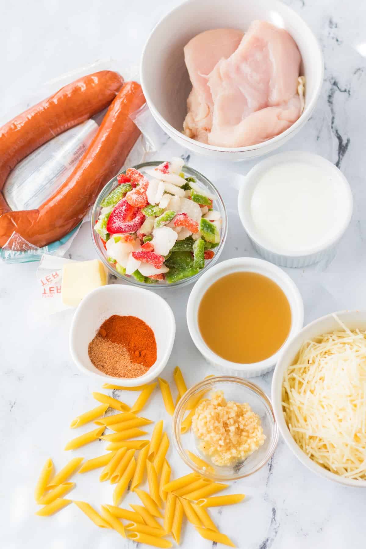 Ingredients for slow cooker Cajun chicken pasta including chicken, sausage, pasta, cream and Cajun seasoning.