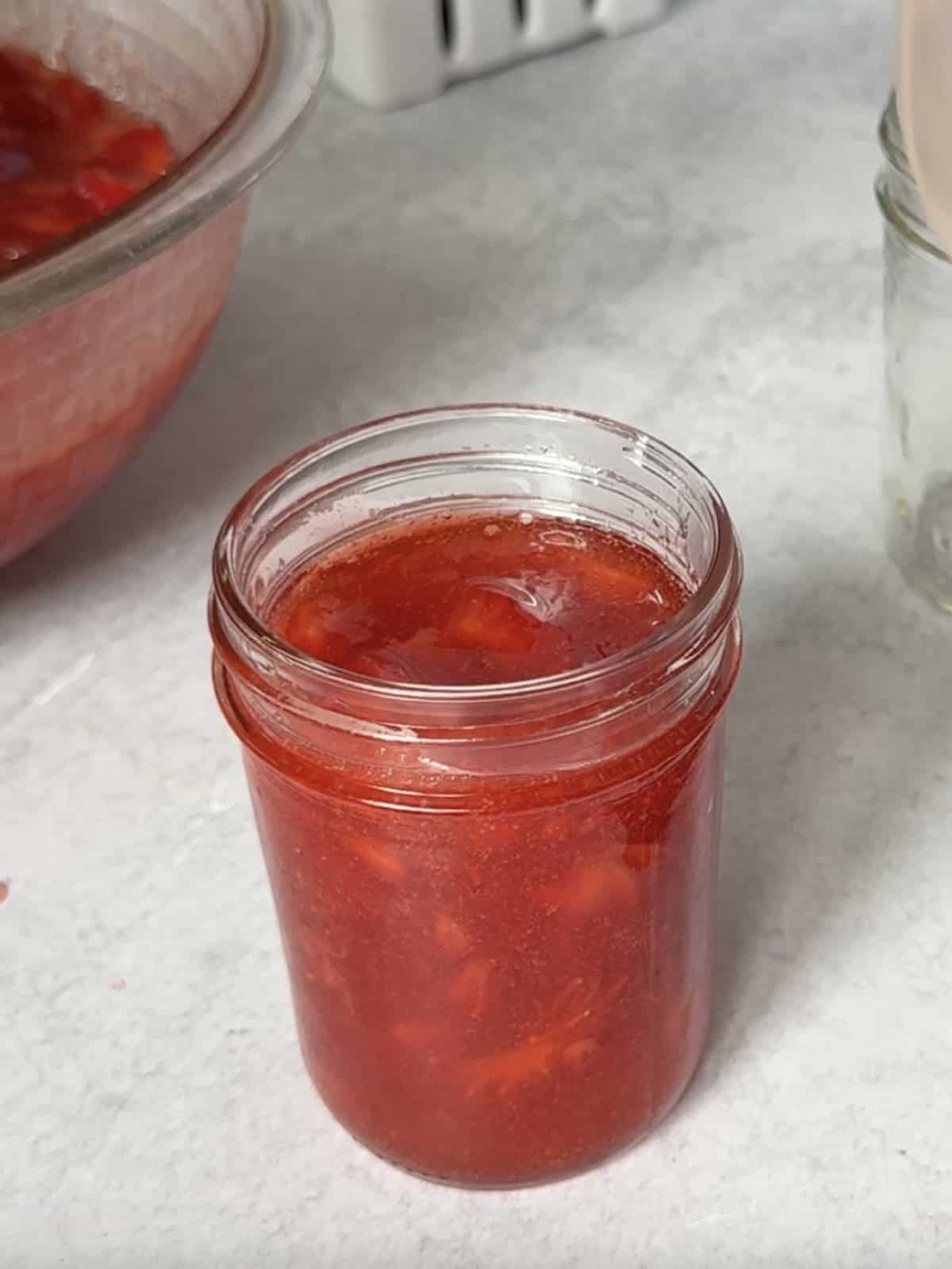 Spooning strawberry freezer jam into jars, leaving ½ inch headspace.