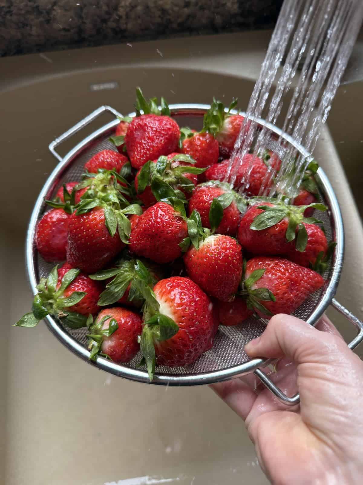 Rinsing ripe strawberries in a strainer.