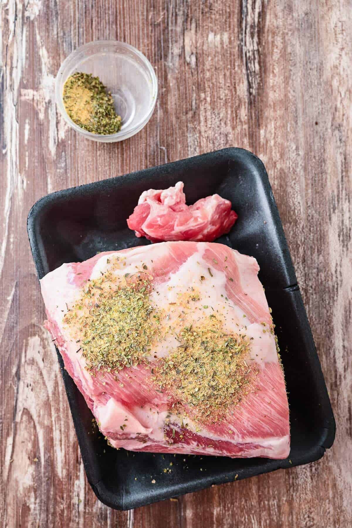 A pork shoulder seasoned with Italian seasoning and garlic salt in a crockpot.