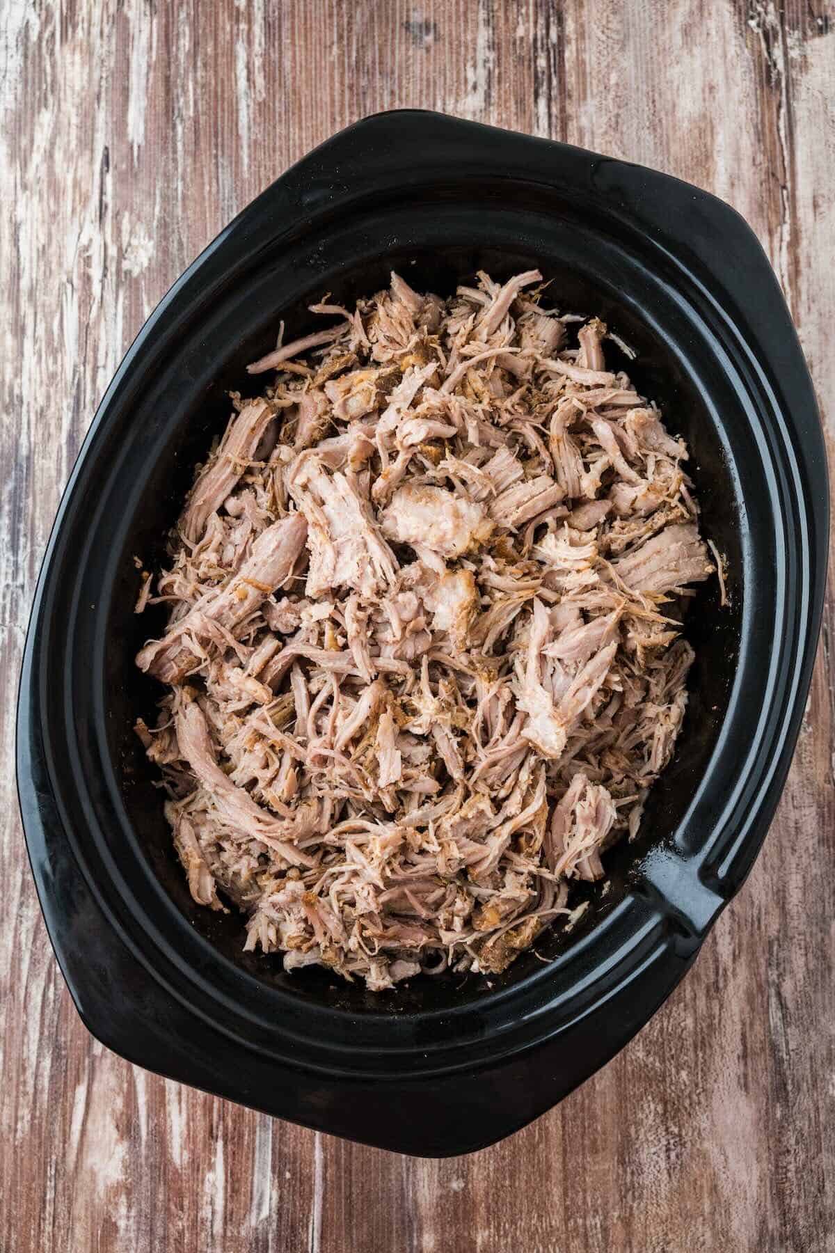 Tender shredded pulled pork in the slow cooker, ready for serving.