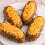 Classic twice baked potatoes topped with cheddar cheese and chives on a serving plate.