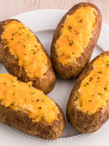 Classic twice baked potatoes topped with cheddar cheese and chives on a serving plate.