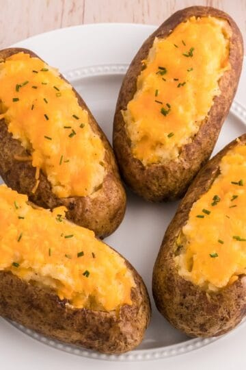 Classic twice baked potatoes topped with cheddar cheese and chives on a serving plate.