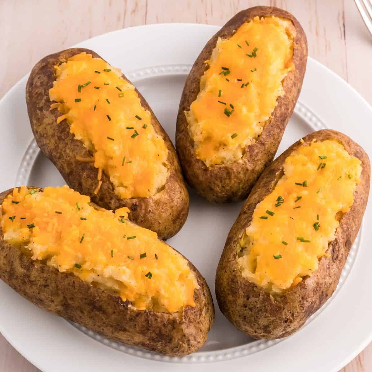 Classic twice baked potatoes topped with cheddar cheese and chives on a serving plate.